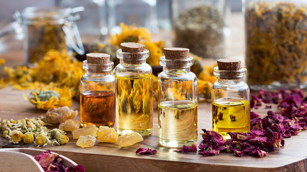Jars of essential oils with dried herbs and flowers on a wooden surface